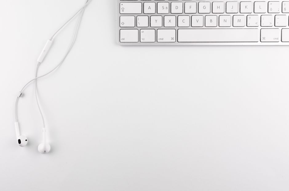 Top view of a minimal white desk setup featuring a keyboard and earphones on a clean background.